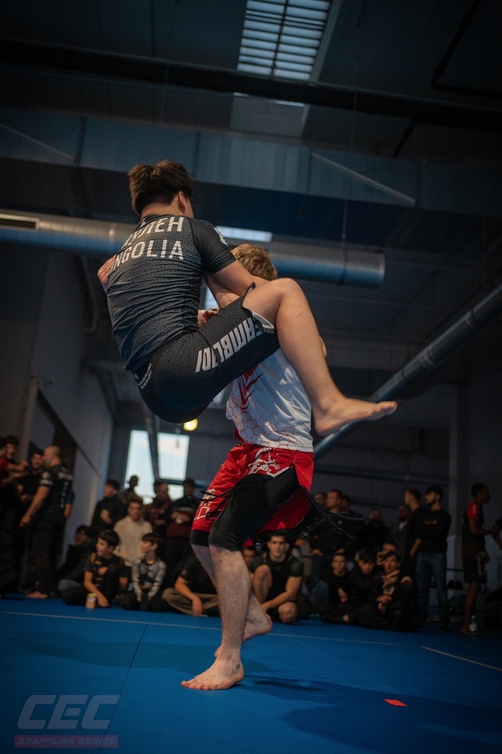 A No-Gi match in progress at Grappling Series 2, with a full room watching